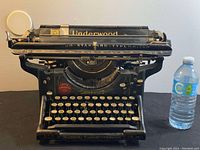 Front angled view of the vintage Underwood Standard Typewriter No.3 showing keys, typebars, and metal frame, with a water bottle for scale.