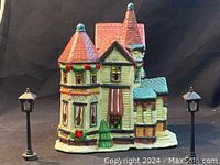 Front view of ceramic Christmas village house with two lamp posts visible, displaying detailed holiday decorations and architecture.
