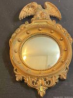 Front view of vintage convex mirror with Federal eagle decorative top, showing gold-toned carved wooden frame and round mirror glass.