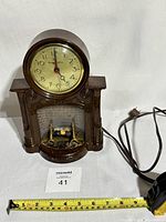 Full view of the brown plastic fireplace clock with power cord and measuring tape showing approximate width.