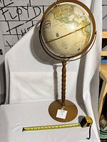 Full view of the 1960s Replogle tall pedestal globe with a measuring tape and background of a white sheet.