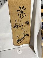 Full view of burlap wall hanging showing Inuit figures and sun design in black ink on natural burlap fabric.