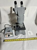 Full view of American Optical professional binocular microscope and separate light control unit on a white surface, with measuring tape for scale.