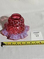 Cranberry glass lampshade with opalescent ruffle edge, diamond quilt pattern and a measuring tape showing width around 7 inches.