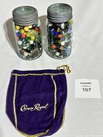 Two aqua green Mason jars filled with colorful assorted marbles next to a purple velvet Crown Royal pouch with gold trim and a Macsold lot number card.