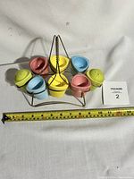Full set of 6 pastel ceramic egg cups and 3 salt and pepper shakers in metal rack with measuring tape showing size approximately 12 cm wide.