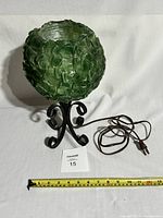 Green textured Lucite globe table lamp on black metal scroll base with power cord and pull chain switch, shown with measuring tape for scale.