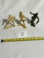 Front view of three vintage Louis Marx plastic toy figures including two soldiers and one cowboy on white background with measuring tape showing approximately 3 to 3.5 inches tall.