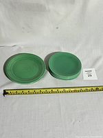 Photo showing six green Fiesta plates arranged in two stacks with measuring tape in front showing size: two larger 7 1/4 inch plates on left and four smaller 6 1/4 inch plates on right.