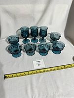 Full view of the set of 6 blue dessert dishes and 3 goblets, arranged on white fabric background, with measuring tape showing size