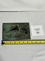 Full view of rectangular brass plaque with a measuring tape showing approximately 6 inches wide by 4 inches tall, placed next to a lot number card.