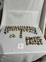 Wide overview showing arranged assortment of approximately 85 small Wade Nursery Rhyme ceramic figurines on a white cloth background, displaying the full lot.