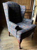 Side angled view of wingback chair with library print fabric upholstery and wooden legs on hardwood floor.