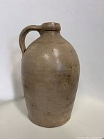 Front view of an antique stoneware jug with one handle, showing the overall shape and condition with no visible markings.