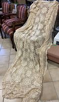 Full view of cream-colored antique/vintage crochet lace bed cover draped over chairs, showing intricate openwork design and size.