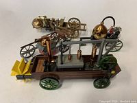 Photo showing two mechanical miniatures: a wooden steam engine tractor model with metal parts and a smaller brass miniature vehicle.