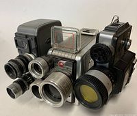 Photo of three vintage 8mm film cameras with various lenses and body styles closely grouped on a white surface.