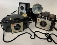 Four vintage 1950s film cameras arranged on a white background: Kodak Premo 135, Brownie Hawkeye, Twin Lens Reflex style camera, and box camera with flash.