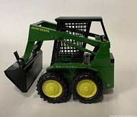 Side view of green John Deere toy skid-steer loader with yellow wheels and black front loader bucket.