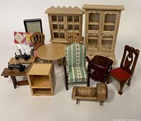 Photo showing a collection of vintage miniature dollhouse furniture items including cabinets, chairs, table, cradle, shelving unit, and miniature sewing machines.
