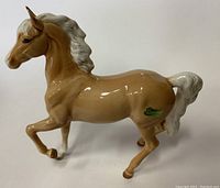 Side view of the prancing palomino horse figurine showing the tan body, white mane and tail, and green label on the right side.