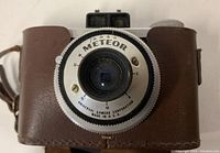 Front view close-up of Universal Meteor camera lens and dial showing markings and text