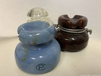 Three antique/vintage porcelain electrical insulators; blue Canadian porcelain insulator, brown glazed porcelain insulator, and clear white insulator with ridged surface.