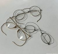 Three pairs of antique spectacles on white surface showing different metal frame types and wear.