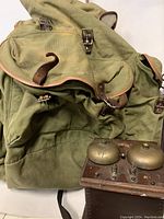 Photo showing the vintage army backpack with leather straps alongside the antique wooden bell phone box.