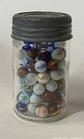 Photo of vintage glass mason jar filled with assorted antique glass marbles with dark metal lid