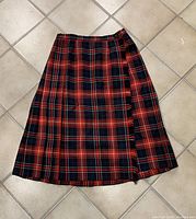 Full view of vintage plaid wool Highland Queen kilt laid flat on tile floor showing pleats and traditional red, black, and navy tartan pattern.
