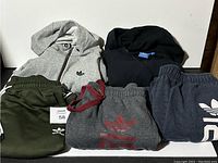 View of all five Adidas items: three pants and two hoodies, displayed together on a table