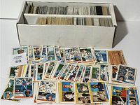 Two-row white storage box fully packed with assorted baseball cards in varying conditions with additional cards spread in front.