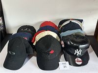 Front view of three rows of baseball caps including black, red, and blue caps with various logos including Oakley, Toronto Blue Jays, and New York Yankees leather cap.