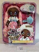 Front view of Na! Na! Surprise Teens Series 2 doll Lila Lamb in original packaging showing doll with long pink braided hair, denim overall, and pink skirt, including accessories like a hairbrush.