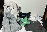Photo showing 2 Nike hoodies and 4 Nike shirts in various colors stacked on a surface.