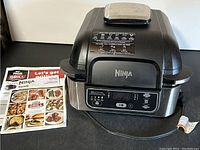 Ninja Foodi air fryer from an angle showing the front control panel and instruction manuals placed beside it.