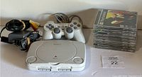 Sony PS One console with two controllers, power and AV cords, and nine PS1 game cases stacked on right side