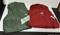 Green Puma pants and red Puma hoodie laid flat for display, showing size and logo details.