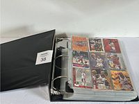 Black three-ring binder partially open displaying plastic pages filled with vintage basketball cards.
