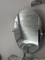 Oval bathroom mirror mounted on wall above sink, showing mirror and chrome mounting hardware with one side missing silver end.