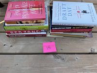 Top-down view of 10 stacked books on a wooden table, titles visible showing a range of topics including business, sports, and self-help, with a pink label marked '18'.