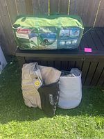 Coleman 8 Person Tent in green Coleman carrying bag with deflated air mattresses in front, shot outside on grass with deck box behind.