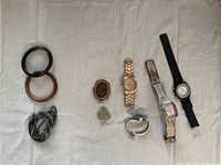 Photo showing two plastic bangles, a silver-tone chain bracelet, two brooches, and four watches with varied style bands on a beige cloth.