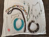 View of the assortment of costume jewelry necklaces laid out on a white cloth showing the variety of styles, colors, and materials.