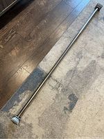 Chrome extendable curtain rod laid flat on carpet and wood floor.