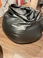 Silver pleather beanbag chair on wooden floor, showing side and front views with smooth shiny synthetic leather surface and natural wrinkles.