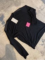 Full view of black long sleeve Merino wool shirt laid flat on carpet, showing leather-like shoulder panels and the stain on sleeve.