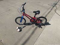 Full side view of the red and blue Raleigh Vibe kids' bike with training wheels attached, showing overall structure and condition.