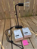 Black metal hanging lamp with exposed Edison bulbs and attached power cord, displayed on wooden deck